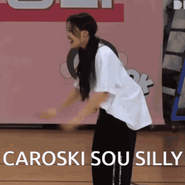 a woman in a white shirt and black pants is standing in front of a sign that says " caroski sou silly "