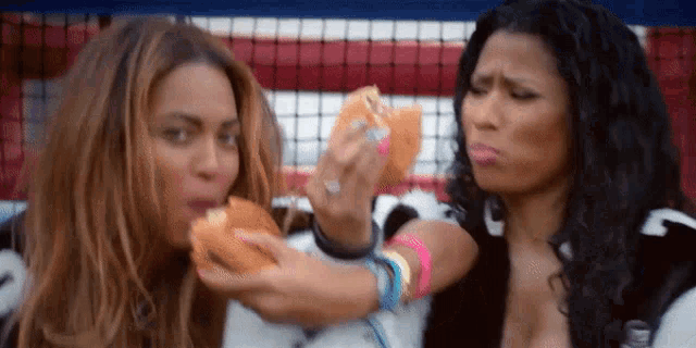 two women are eating hamburgers and one of them is making a face