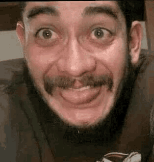 a man with a beard is making a funny face and sticking his tongue out .