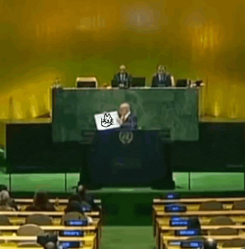 a man is sitting at a podium with a cat on his laptop .
