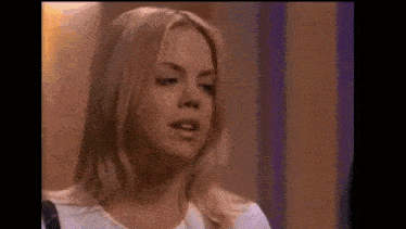 a woman with blonde hair is standing in front of a purple wall and talking to someone .
