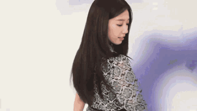 a woman with long black hair is standing in front of a purple background wearing a black and white dress .
