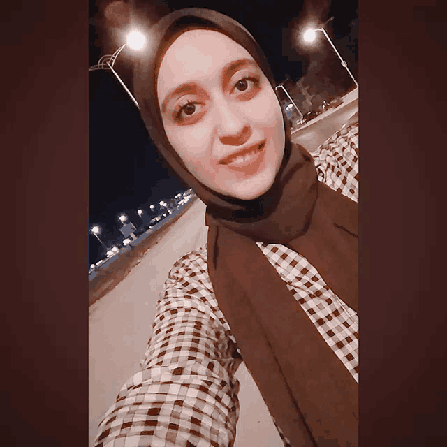 a woman wearing a hijab and a plaid shirt smiles for a picture