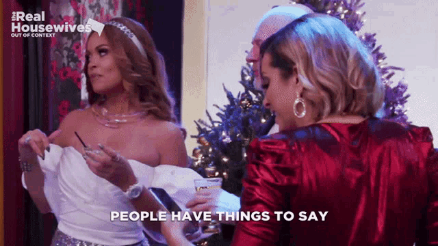 two women are standing in front of a christmas tree with the words " people have things to say " on the bottom