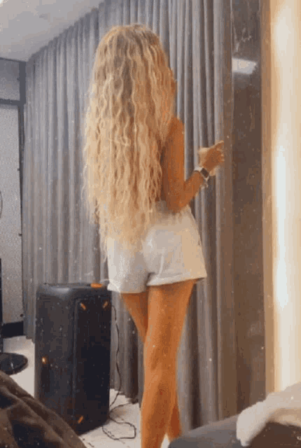 a woman with long blonde hair and shorts is standing in front of a curtain