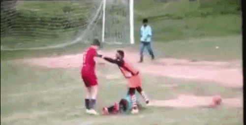 two soccer players are fighting on a field while a man watches .