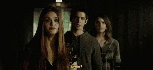 a group of people are standing next to each other in a dark room and a woman is asking lydia .