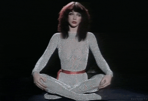a woman in a white bodysuit is sitting in a lotus position with her legs crossed