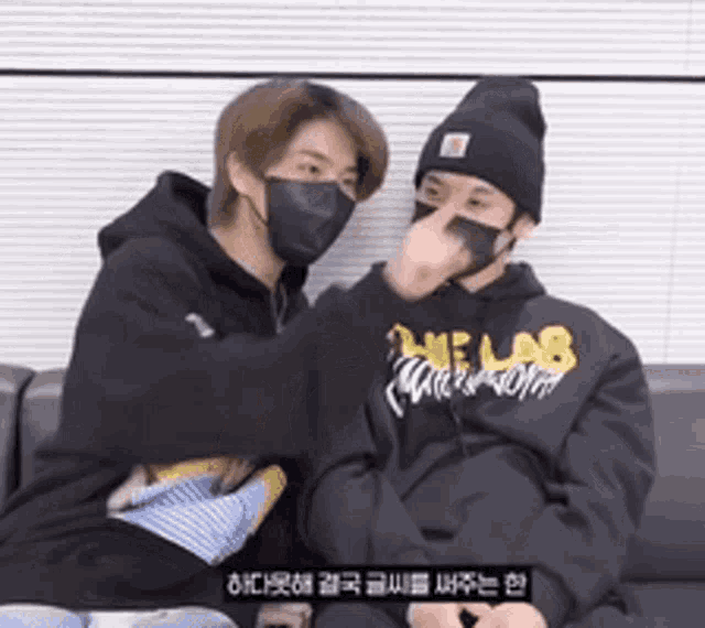 two men wearing masks are sitting on a couch