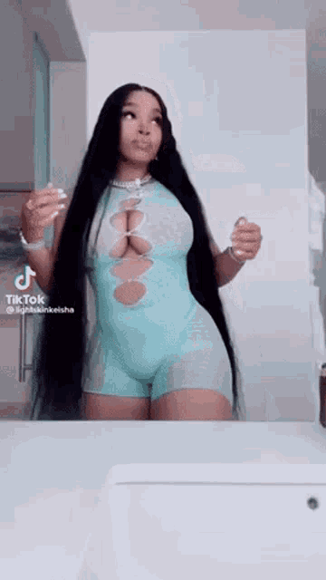 a woman in a blue bodysuit is standing in front of a bathroom mirror .