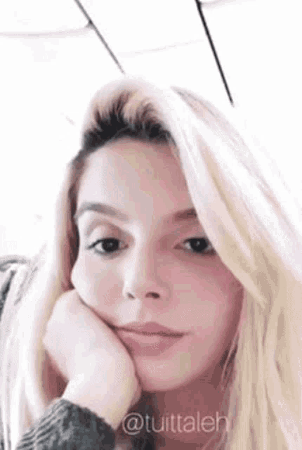 a woman with blonde hair is holding her hand to her face .