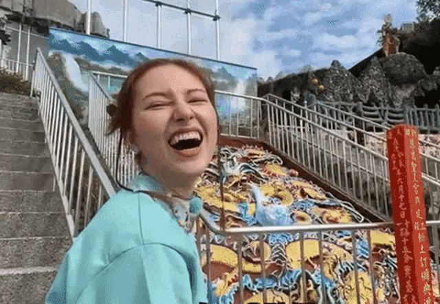 a woman in a blue shirt is laughing in front of stairs