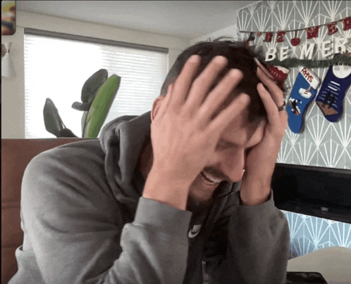 a man covering his face with his hands in front of a christmas banner that says be mine