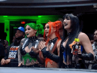 three women are standing next to each other in front of a crowd and one of them has green hair .