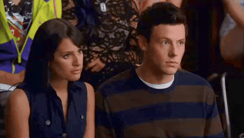 a man and a woman are sitting next to each other in a crowd . the man is wearing a striped shirt .
