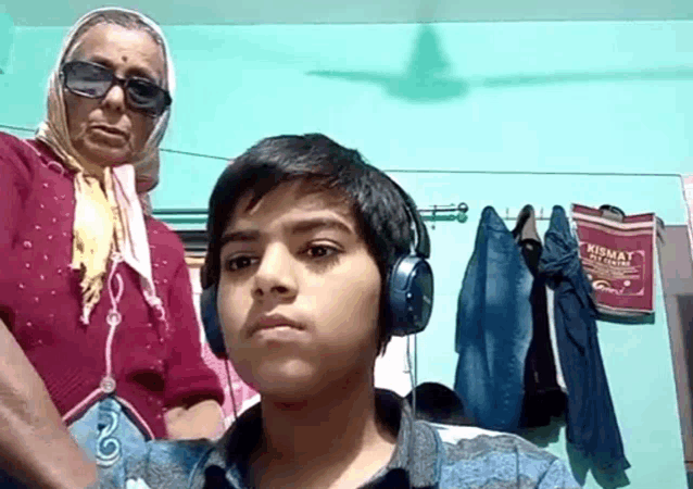 a boy wearing headphones stands in front of a woman wearing sunglasses