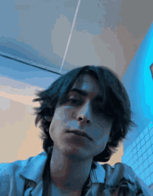 a young man with long dark hair is taking a selfie in a bathroom .