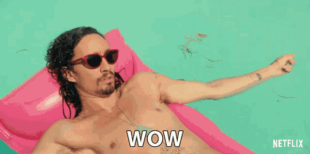 a shirtless man is laying on a pink float with the word wow written on it