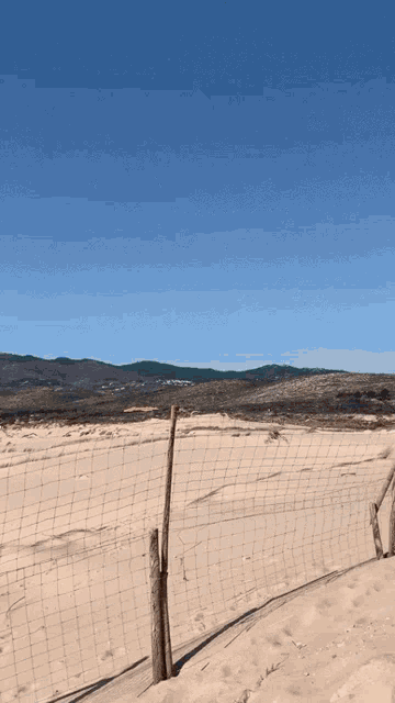 a fence surrounds a sandy area with mountains in the distance