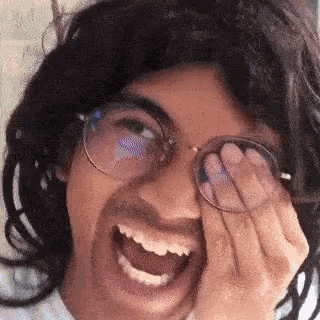 a man wearing glasses and a wig is laughing while covering his eyes .