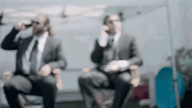 two men in suits are sitting in chairs drinking beer