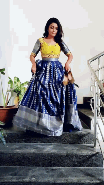 a woman in a blue and silver dress is standing on stairs holding a pair of shoes