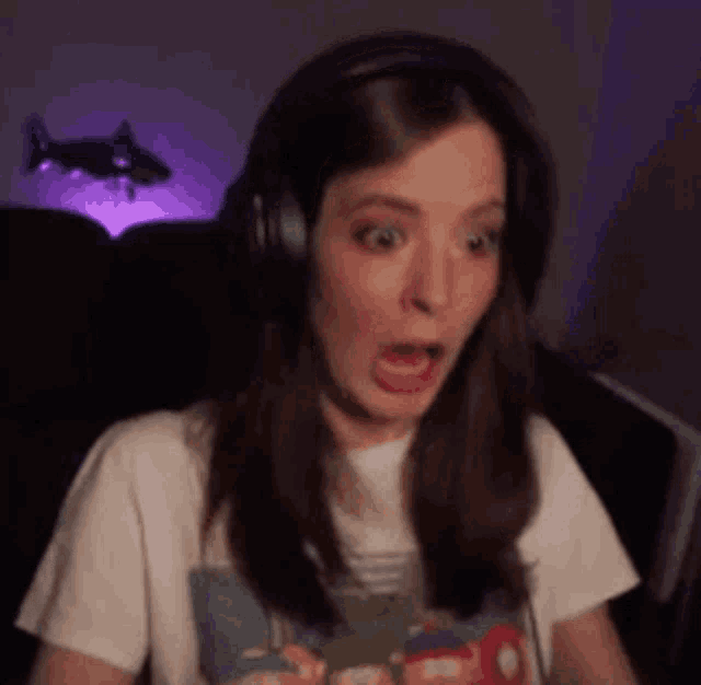 a woman is wearing headphones and making a surprised face while playing a video game .