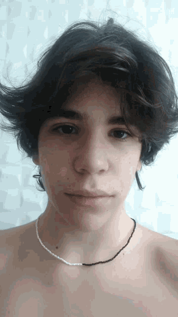 a young man wearing a black and white necklace looks at the camera