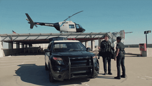 two police officers are standing in front of a helicopter that says n007pd on it