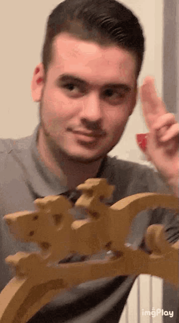 a man in a gray shirt is holding a wooden horse and pointing at it