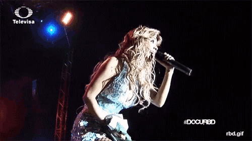 a woman is singing into a microphone on a television screen