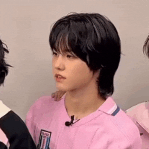a young boy with black hair is wearing a pink shirt and a microphone .