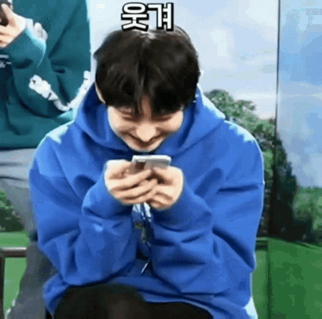 a young man in a blue hoodie is holding a cell phone in his hands .