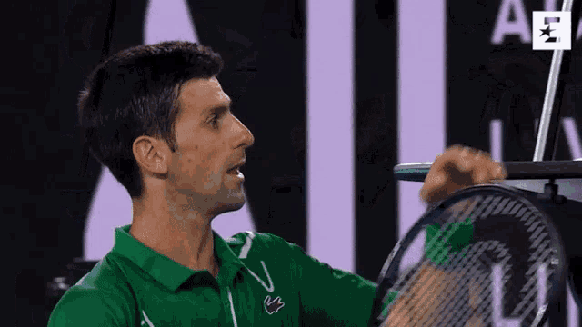 a man in a green shirt with a lacoste logo on it is holding a tennis racquet