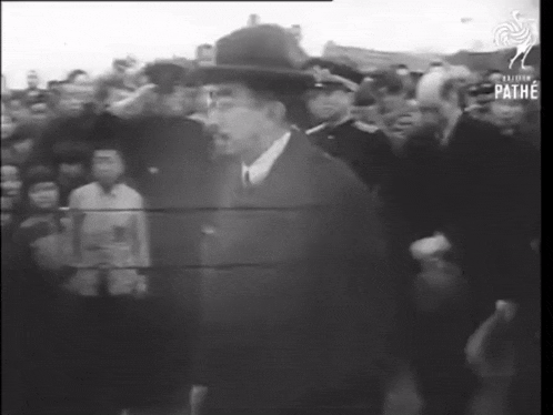 a man in a hat stands in front of a crowd in a black and white photo .