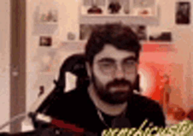 a man with a beard and glasses is sitting in front of a microphone in a room .