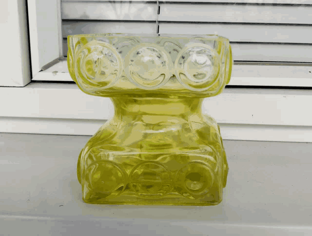 a yellow vase sits on a window sill in front of blinds