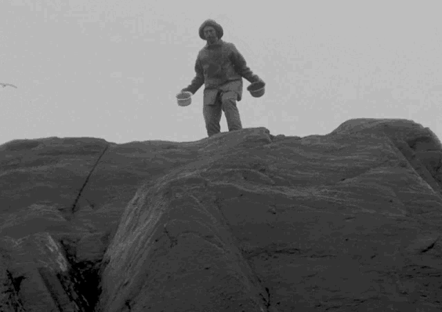a black and white photo of a man standing on top of a rock