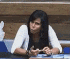 a woman is sitting at a table with a tissue box in the background and making a funny face .