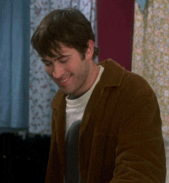 a man in a brown jacket is smiling in front of a window