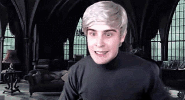 a man in a wig is sitting in a living room with a lot of windows .