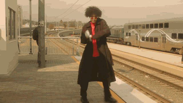 a man in a trench coat stands on a train platform near a metro train
