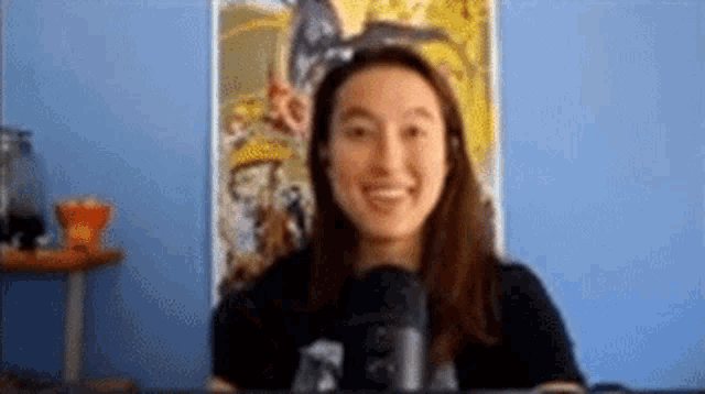 a woman is smiling in front of a microphone while sitting in front of a blue wall .