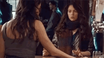 two women are sitting at a bar talking to each other . one of the women is holding another woman 's hand .