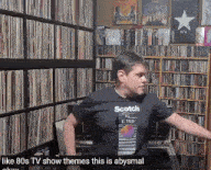 a man wearing a scotch t-shirt is standing in front of a bookshelf