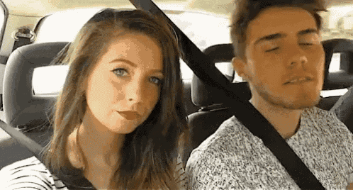 a man and a woman are sitting in a car with their eyes closed . the woman is wearing red lipstick .