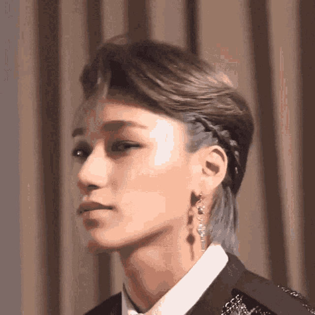 a close up of a person 's face with a braided hairdo and earrings .