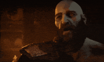 a bald man with a beard holds his hand to his chin