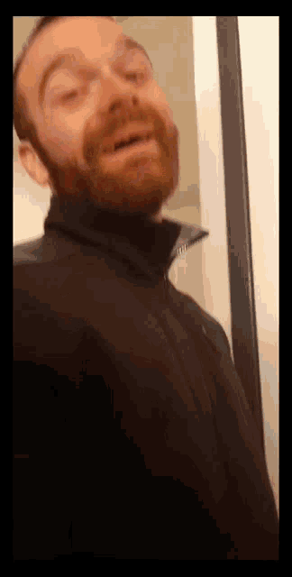 a man with a beard is wearing a black jacket and making a funny face
