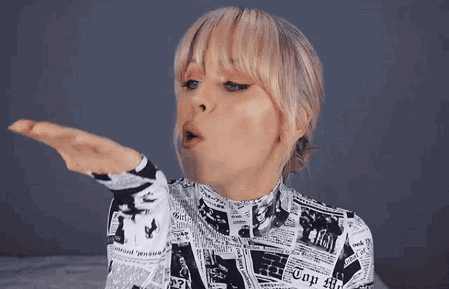 a woman blowing a kiss wearing a shirt with newspaper headlines